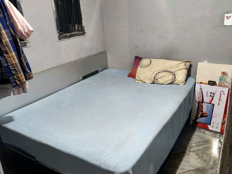 A compact bedroom featuring tiled flooring and windows with security bars, currently requiring cosmetic updates and wall repairs to improve the overall condition.