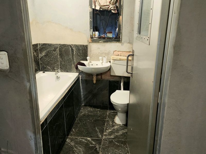 A compact bathroom featuring a bathtub, pedestal sink, and toilet, currently requiring significant renovation and finishing of the wall surfaces.