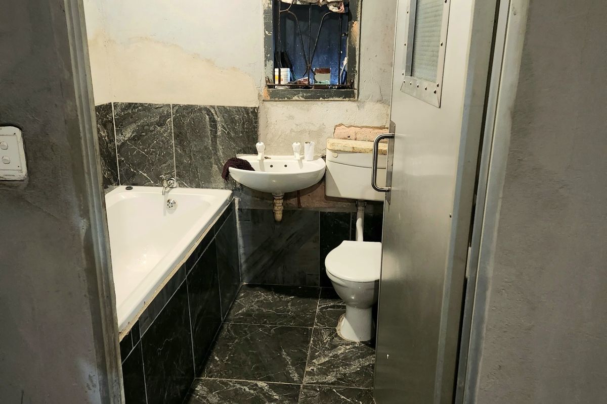 A compact bathroom featuring a bathtub, pedestal sink, and toilet, currently requiring significant renovation and finishing of the wall surfaces.