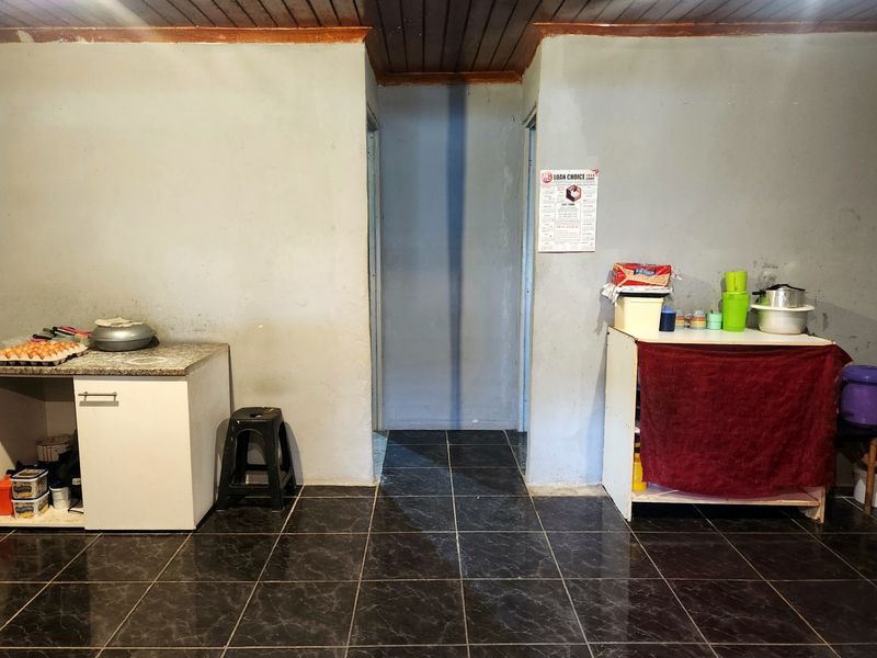 A functional kitchen area featuring dark tiled flooring, timber ceiling paneling, and basic base cabinetry units.