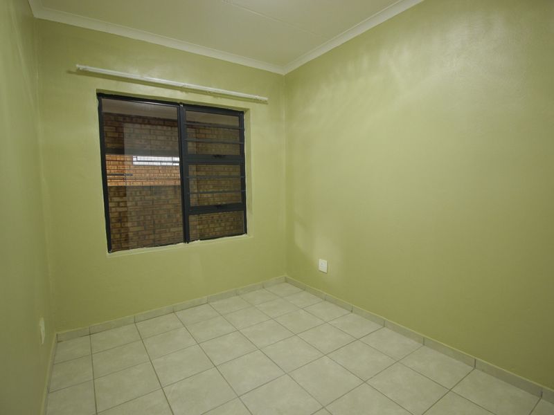 An empty bedroom featuring tiled flooring, light green walls, and a window fitted with security bars.