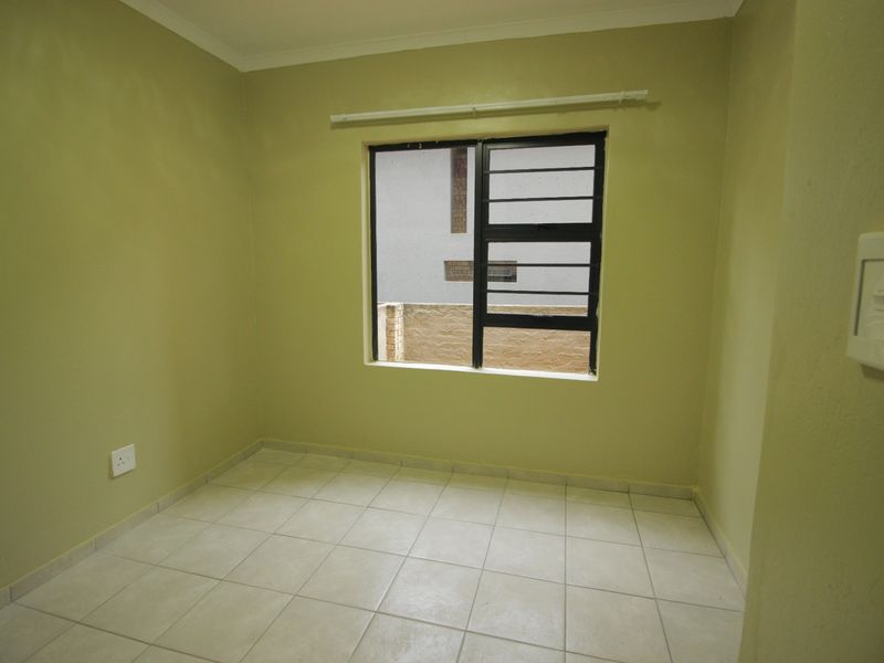 A clean, empty bedroom featuring neutral wall paint, tiled flooring, and a window fitted with security bars and a curtain rail.