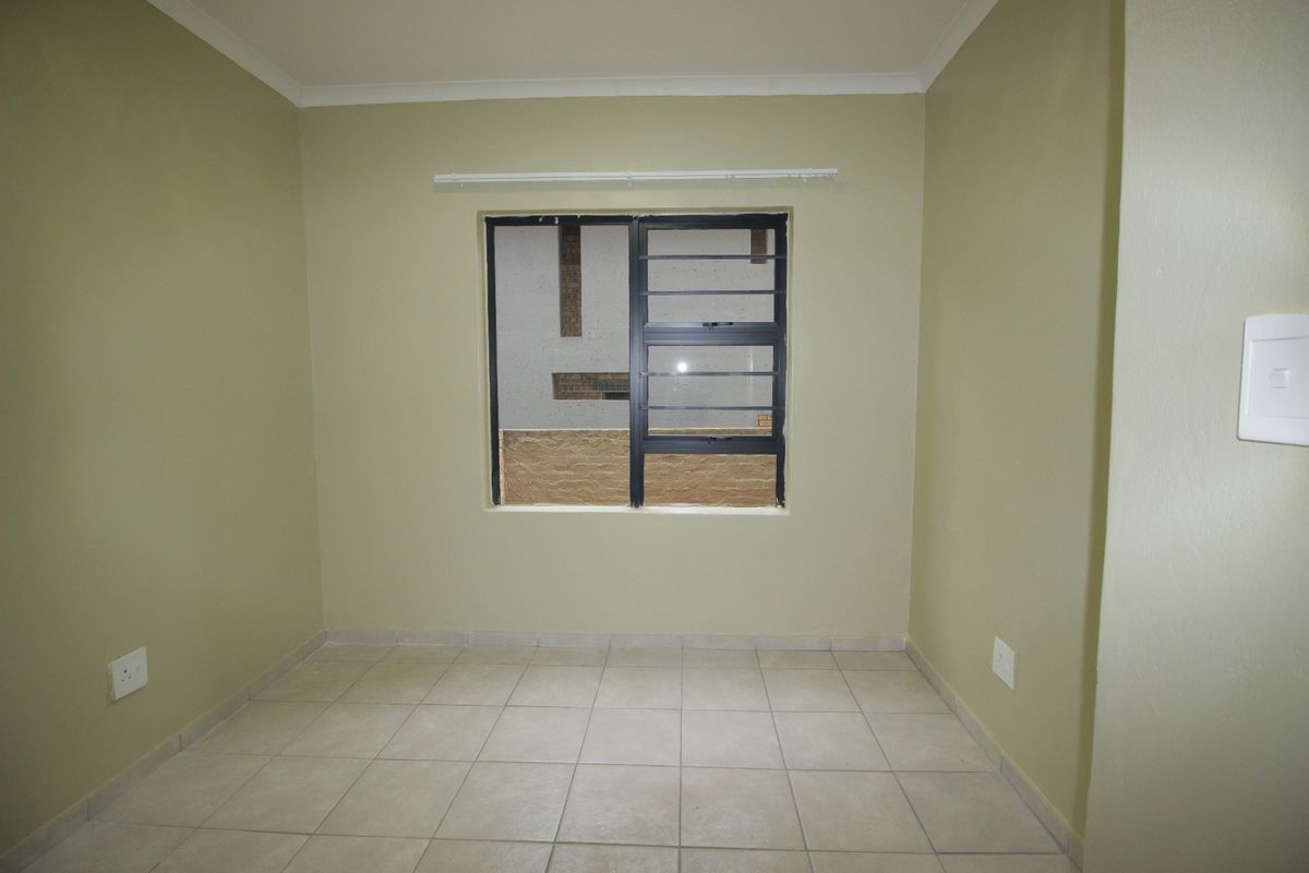 An empty bedroom featuring neutral-toned walls, tiled flooring, and a horizontal sliding window with security bars.