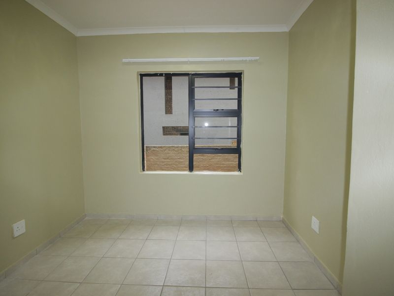An empty bedroom featuring neutral-toned walls, tiled flooring, and a horizontal sliding window with security bars.