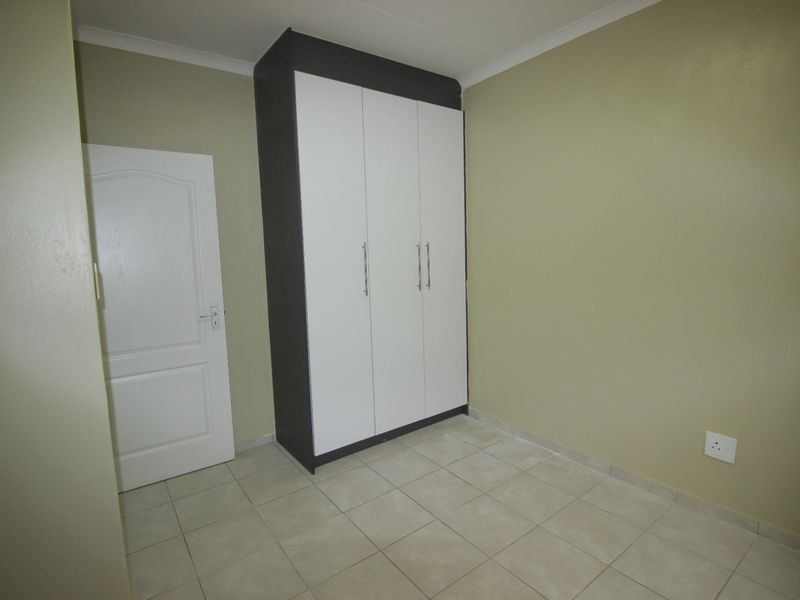 A clean, empty bedroom featuring neutral wall paint, tiled flooring, and a modern built-in wardrobe with white doors and a dark frame.