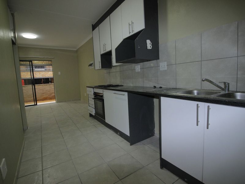 An empty kitchen featuring built-in cabinetry, a stainless steel sink, and a built-in oven, with direct access to an outdoor balcony area.