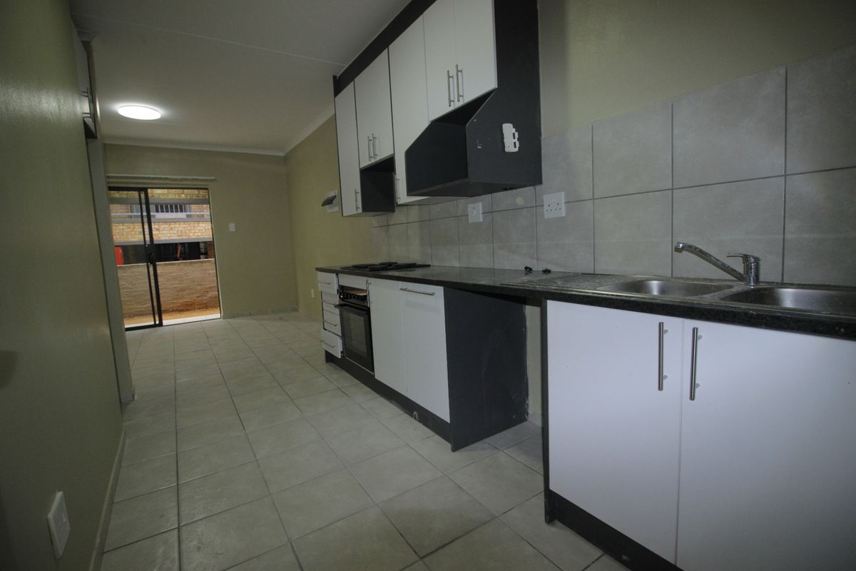 An empty kitchen featuring built-in cabinetry, a stainless steel sink, and a built-in oven, with direct access to an outdoor balcony area.