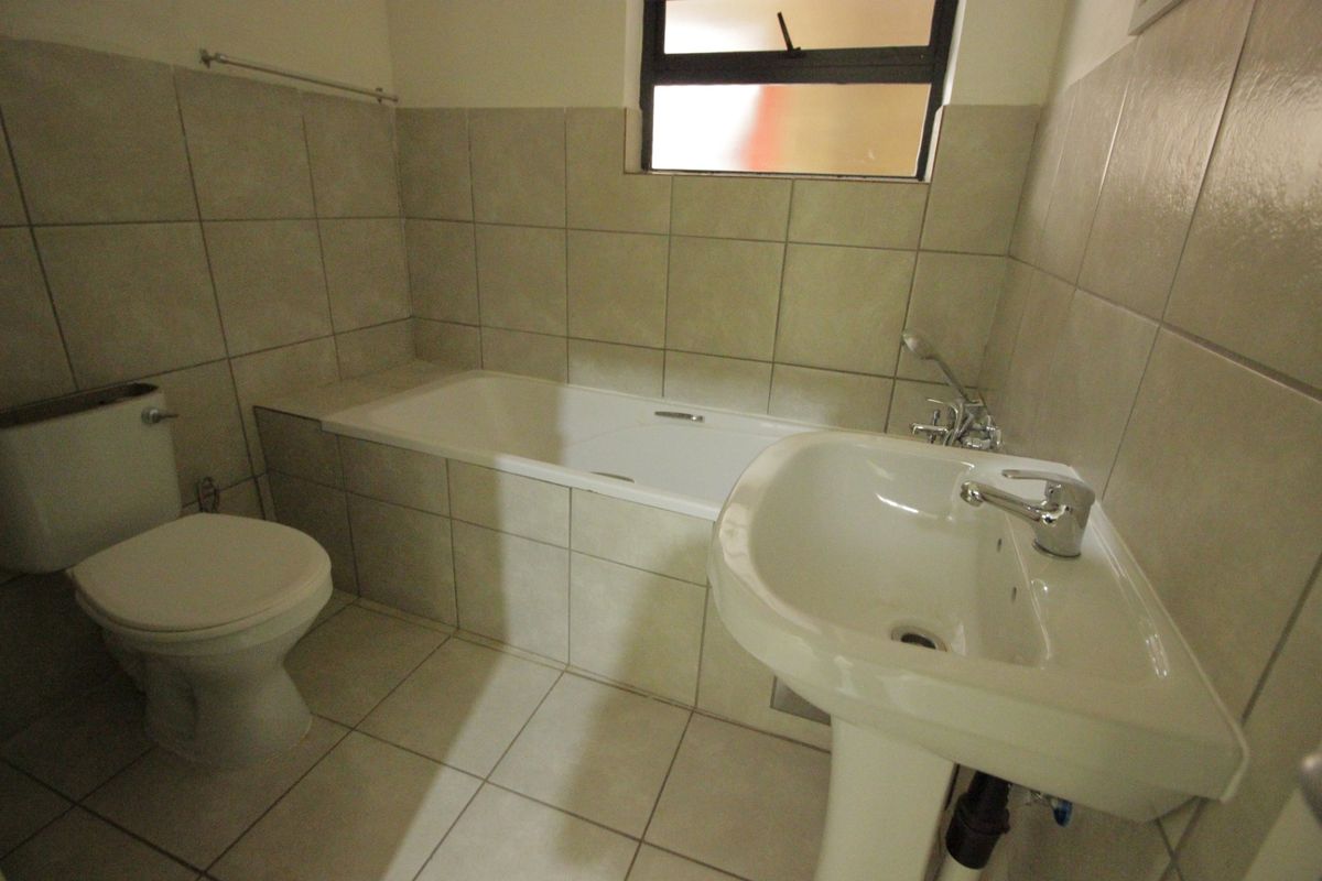 A functional bathroom featuring a pedestal washbasin, bathtub, and toilet with neutral wall and floor tiling.