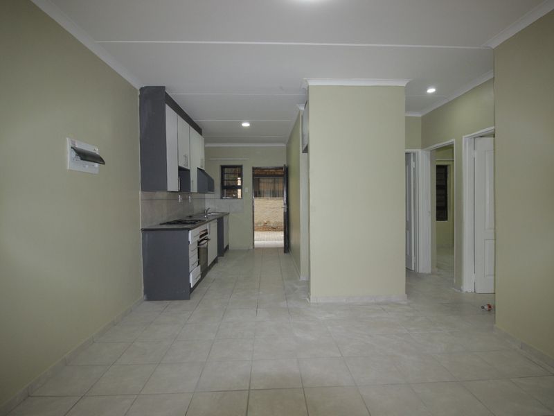 An open-plan living and kitchen area featuring tiled flooring, neutral walls, and built-in cabinetry with integrated appliances.