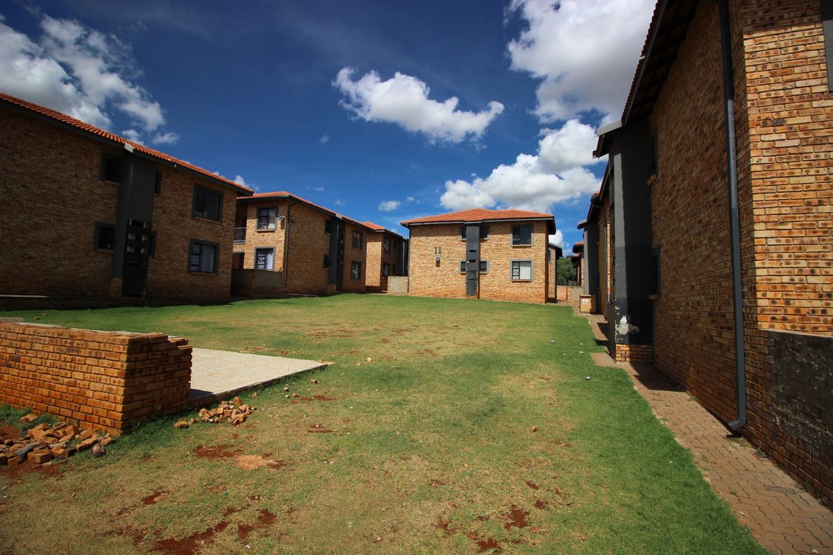 A view of the communal garden area between apartment blocks, featuring face brick facades, tiled roofs, and paved walkways.
