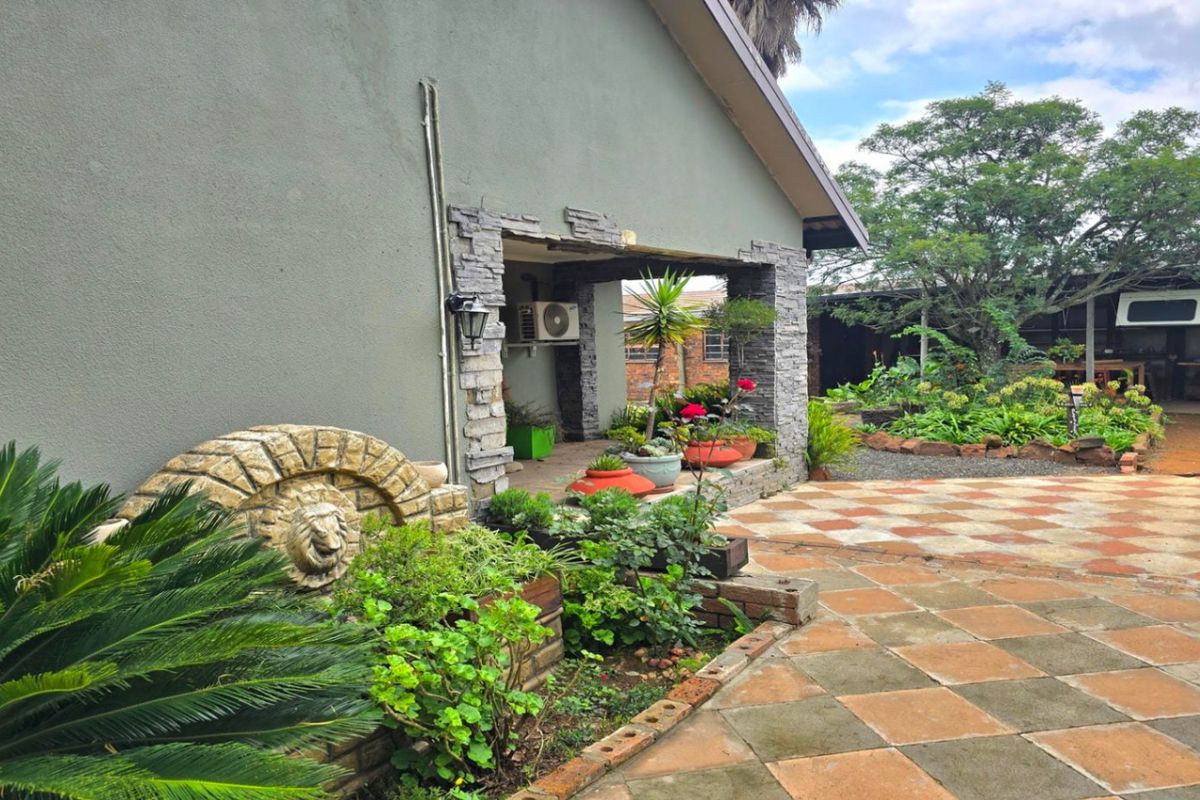 Rear exterior view featuring a covered patio area with stone cladding, paved courtyard, and established garden landscaping.
