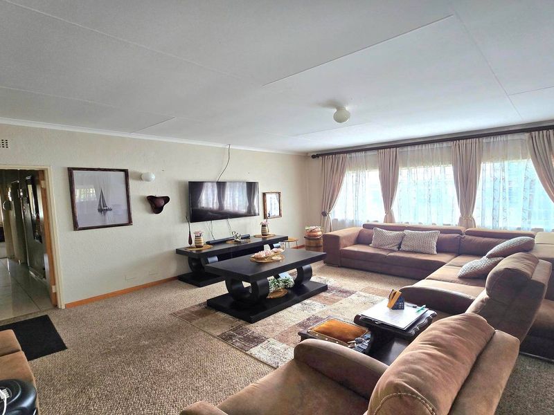A spacious living room featuring neutral wall tones, carpeted flooring, and large windows with curtain treatments, offering a comfortable and functional living space.