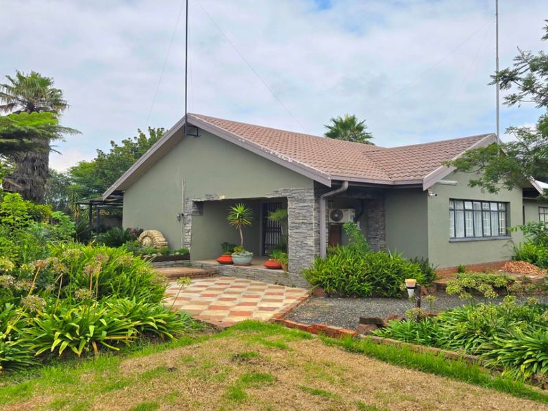 A well-maintained single-story home featuring a tiled roof, stone-clad entrance pillar, and a paved patio area set within a landscaped garden.