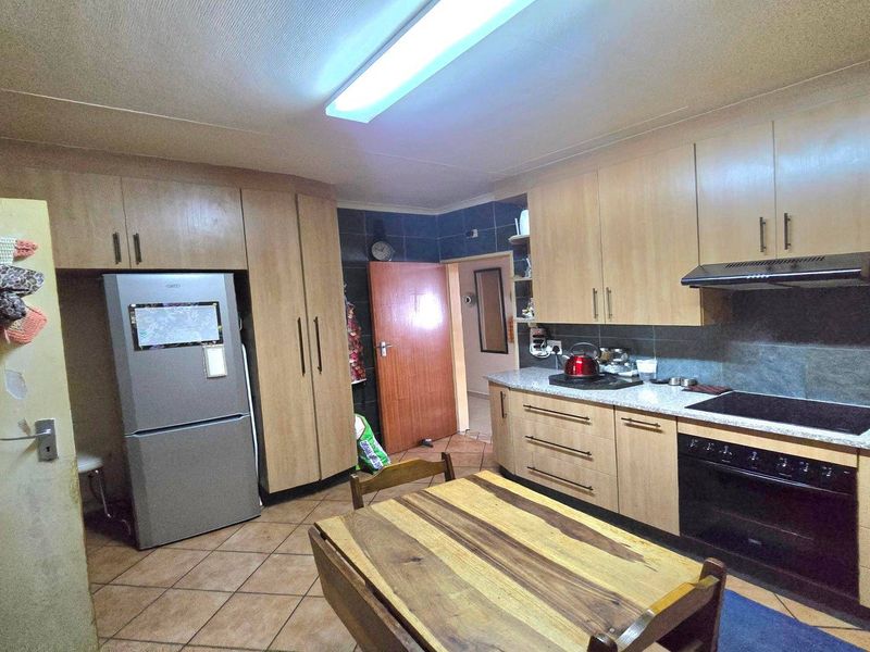 Functional kitchen featuring light wood-tone cabinetry, dark tiled backsplash, integrated oven and hob, and durable tiled flooring.