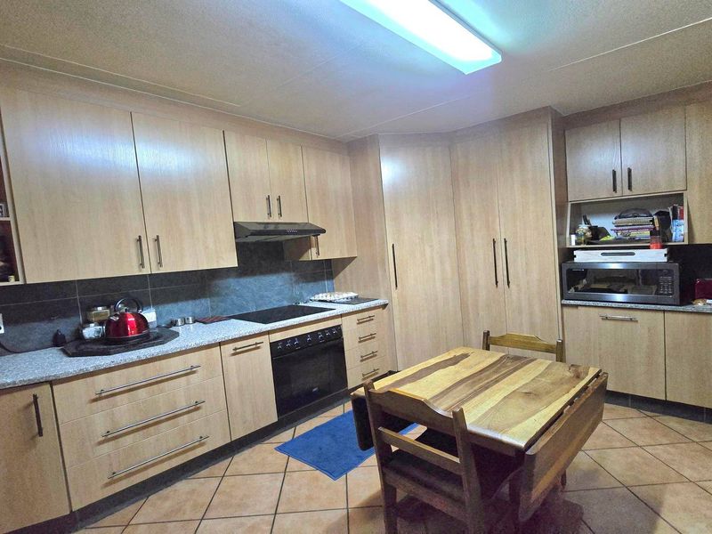 Functional kitchen featuring light wood-finish cabinetry, stone-look countertops, built-in oven, electric hob, and tiled flooring.