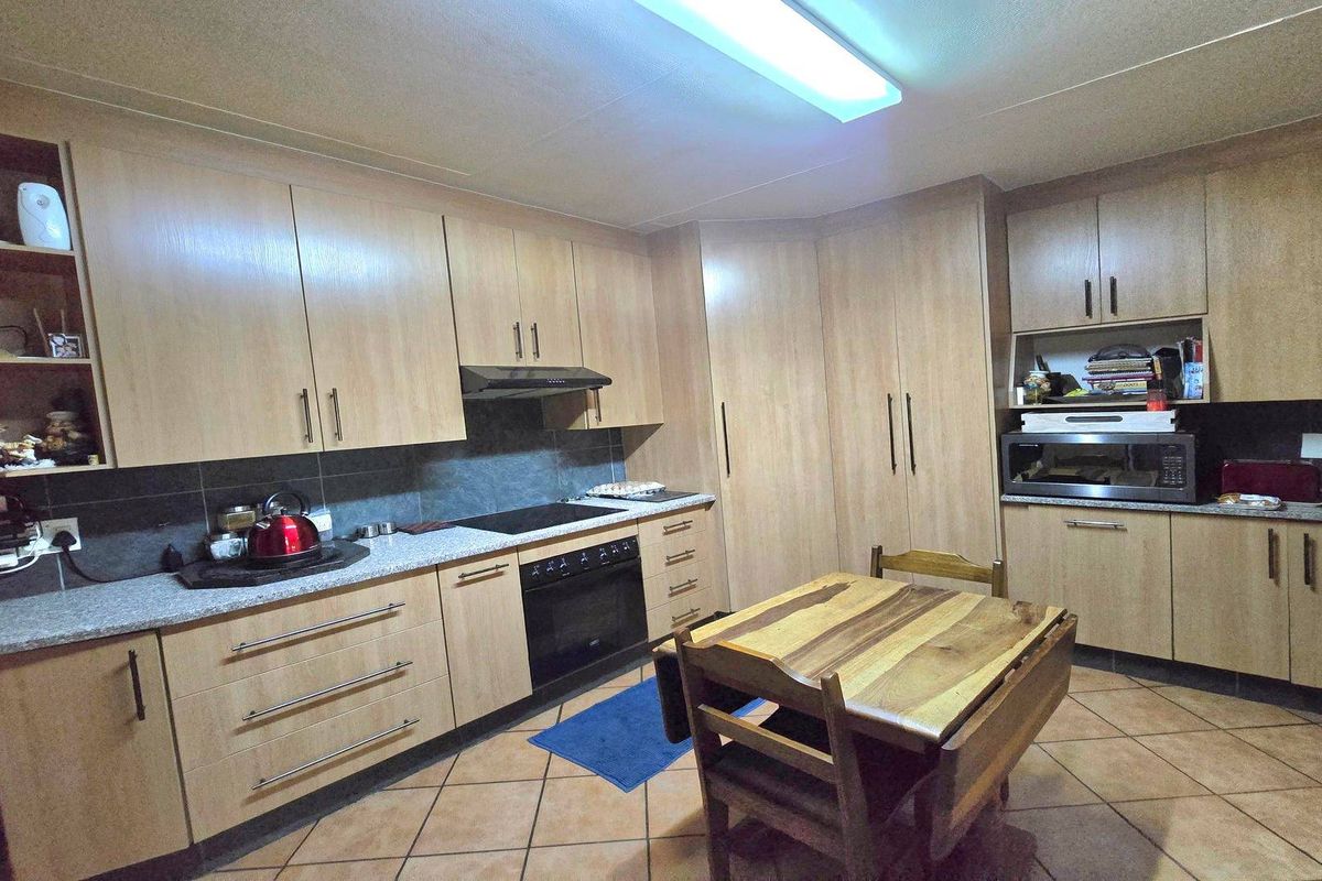 Functional kitchen featuring light wood-finish cabinetry, stone-look countertops, built-in oven, electric hob, and tiled flooring.