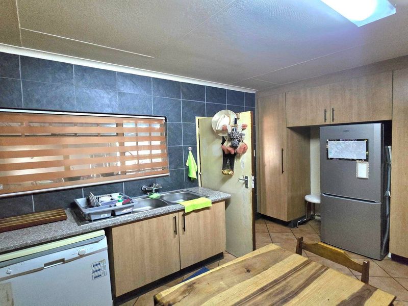 Functional kitchen featuring laminate cabinetry, granite-look countertops, a stainless steel double sink, and tiled splashbacks with ample built-in storage.