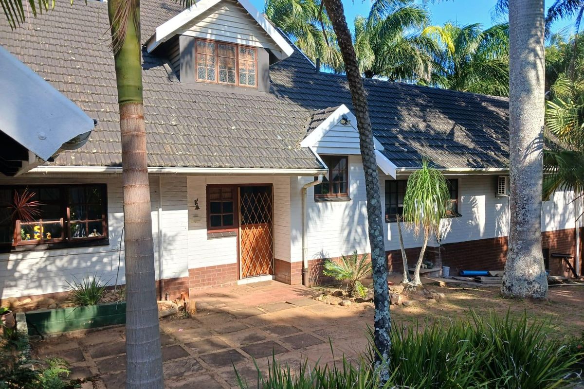 Rear view of a house featuring a tiled roof, brick and painted facade, dormer window, and a paved patio area surrounded by established garden.