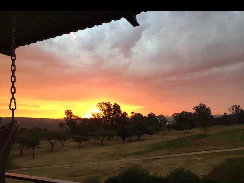 A scenic sunset view overlooking a landscaped estate or golf course, captured from a covered patio area.