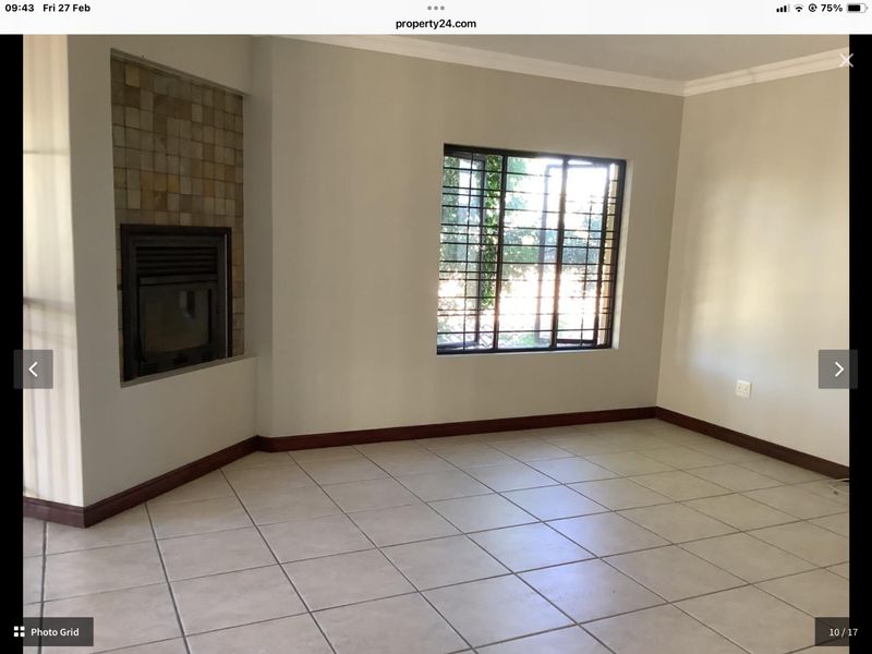An empty living room featuring tiled flooring, a built-in fireplace with a stone tile surround, and a window fitted with security bars.