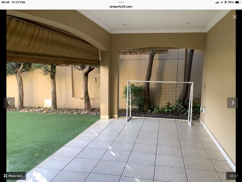 A covered patio area featuring tiled flooring, recessed lighting, and a retractable awning, overlooking a small garden space.