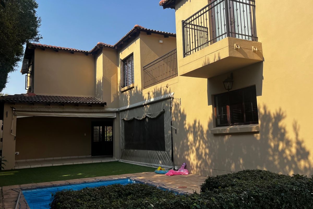 Rear view of the property featuring a swimming pool, covered patio area, and an upper-level balcony with wrought iron railings.
