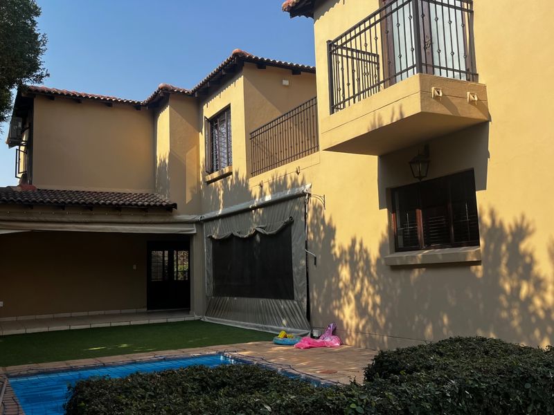 Rear view of the property featuring a swimming pool, covered patio area, and an upper-level balcony with wrought iron railings.