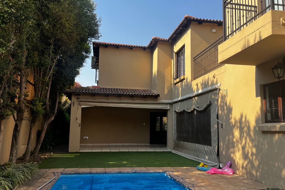 Rear view of the property featuring a swimming pool, covered patio area with retractable awning, and a second-story balcony with wrought iron railings.
