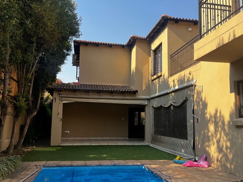 Rear view of the property featuring a swimming pool, covered patio area with retractable awning, and a second-story balcony with wrought iron railings.