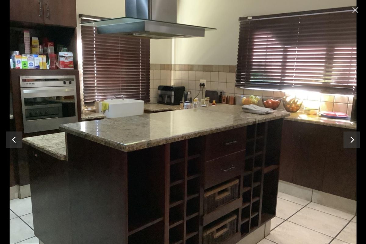 A functional kitchen featuring dark wood cabinetry, granite countertops, a central island with built-in wine storage, and a stainless steel extractor fan.