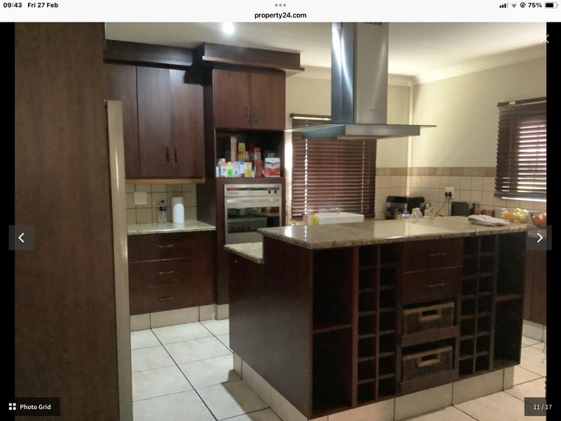 A functional kitchen featuring dark wood cabinetry, granite countertops, a built-in oven, and a stainless steel extractor fan with tiled flooring.