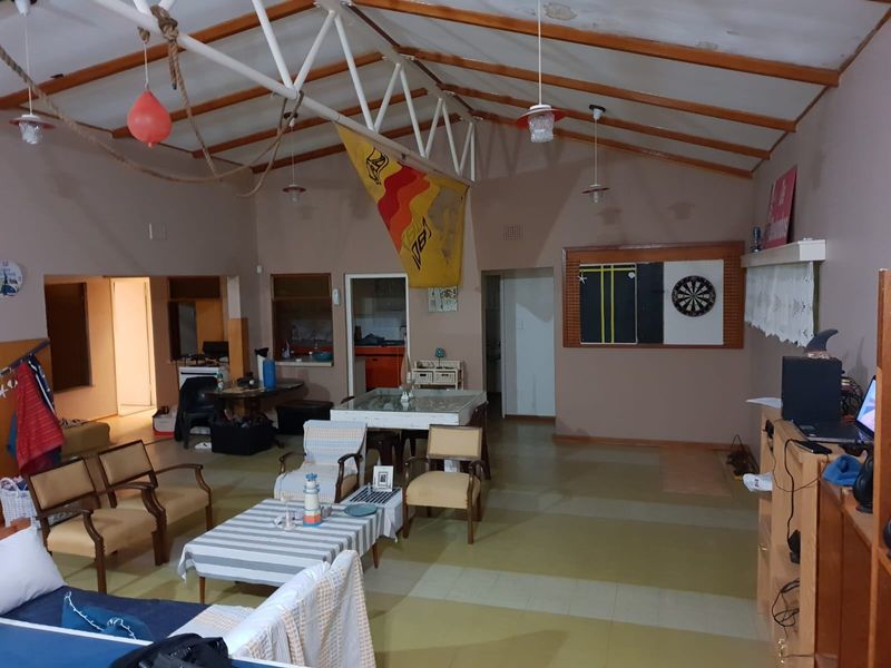 Spacious open-plan living area featuring exposed roof trusses, vaulted ceilings, and vinyl flooring, with visible signs of ceiling wear requiring maintenance.