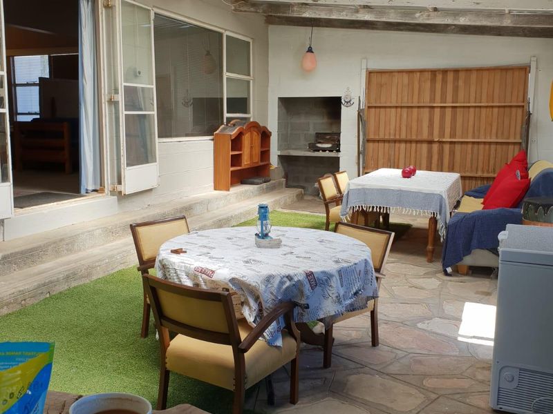 Covered outdoor patio area featuring a built-in braai, stone flooring, and timber ceiling, providing a versatile space for outdoor dining and entertainment.