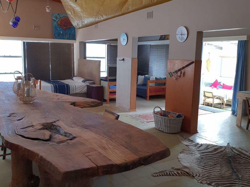 Spacious open-plan living area featuring exposed timber roof trusses, tiled flooring, and multiple partitioned bedroom alcoves with direct access to an outdoor patio.