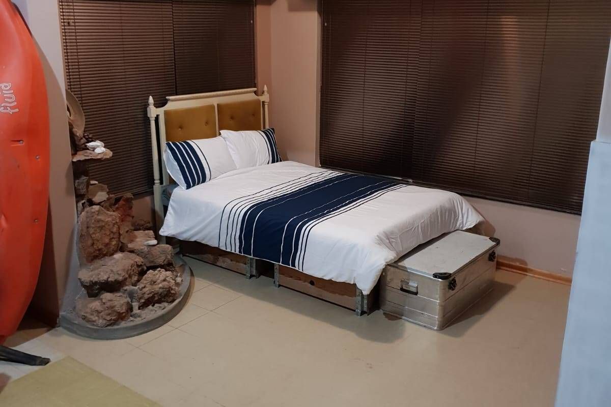 A bedroom featuring venetian blinds and a ventilation grille, with visible wear on the flooring surfaces.