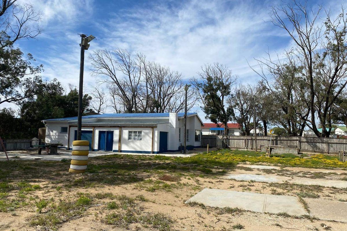 Rear view of the property featuring a single-story structure with a metal roof, concrete patio area, and a large, unlandscaped backyard with timber fencing.