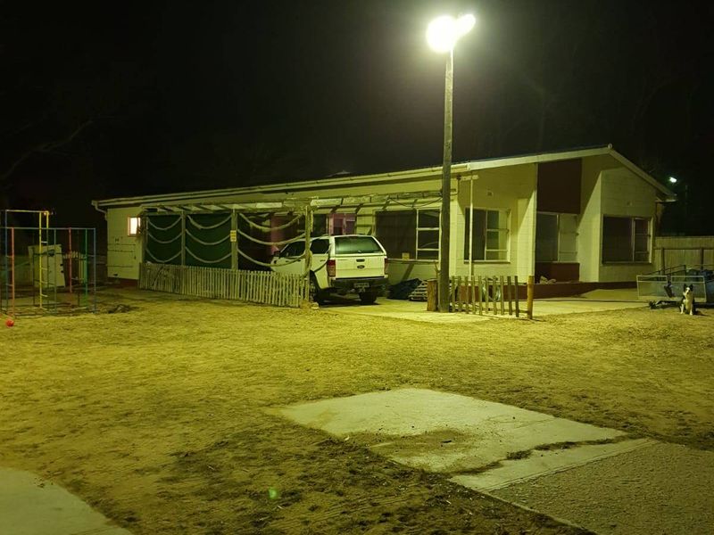 Night view of the rear exterior of the house, featuring a covered patio area, concrete paving, and outdoor floodlighting.