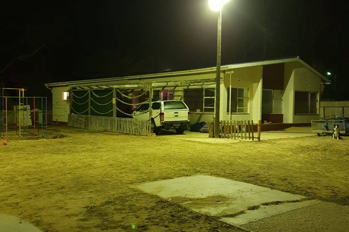 Night view of the rear exterior of the house, featuring a covered patio area, concrete paving, and outdoor floodlighting.