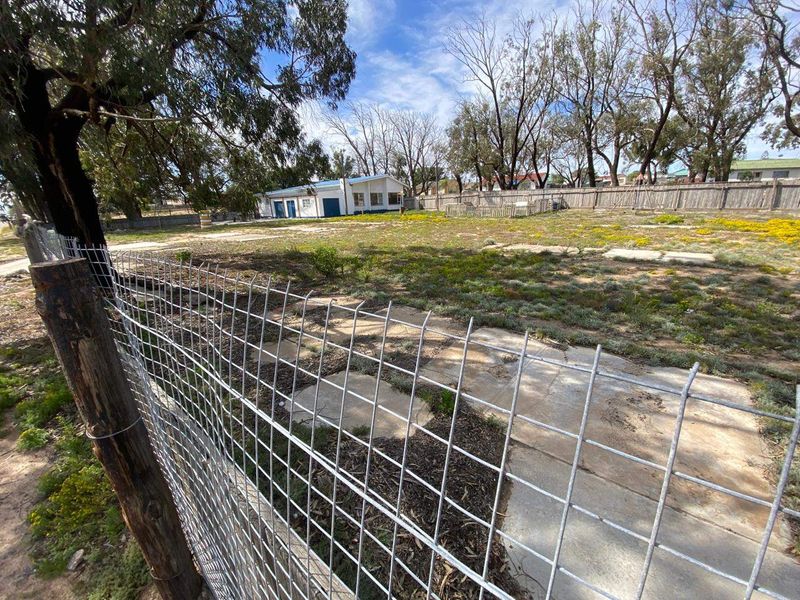 A spacious rear yard featuring wire mesh fencing, timber posts, and scattered paving stones, offering significant potential for landscaping and outdoor development.