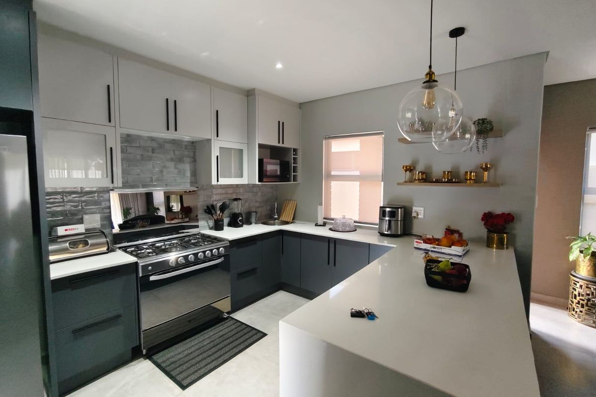 Modern kitchen featuring two-tone cabinetry, quartz countertops, a gas stove with extractor, and stylish pendant lighting over a breakfast peninsula.