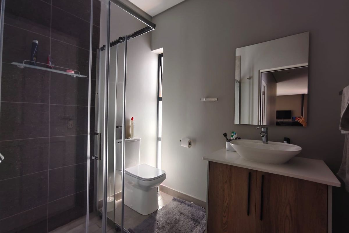 Modern bathroom featuring a glass-enclosed shower, a contemporary vessel sink on a wood-finish vanity, and a wall-mounted mirror.