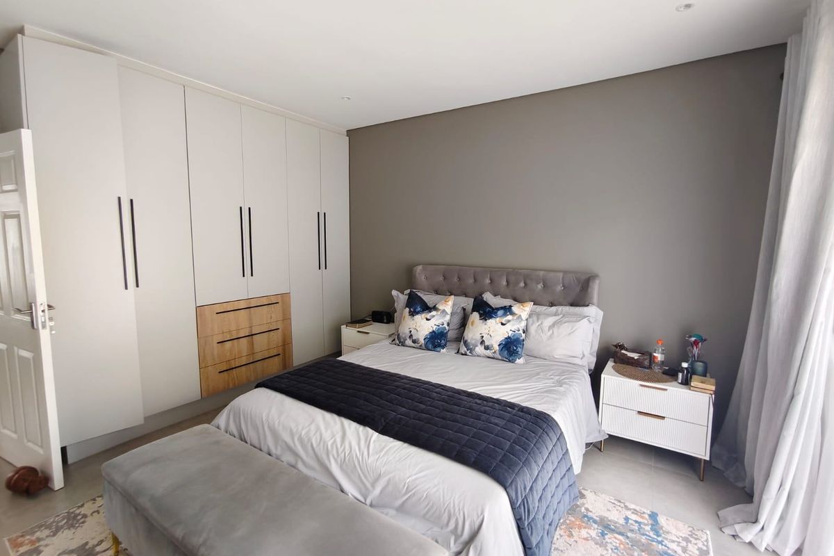 A modern, well-maintained bedroom featuring extensive built-in wardrobes with integrated drawers, neutral wall tones, and sleek tiled flooring.