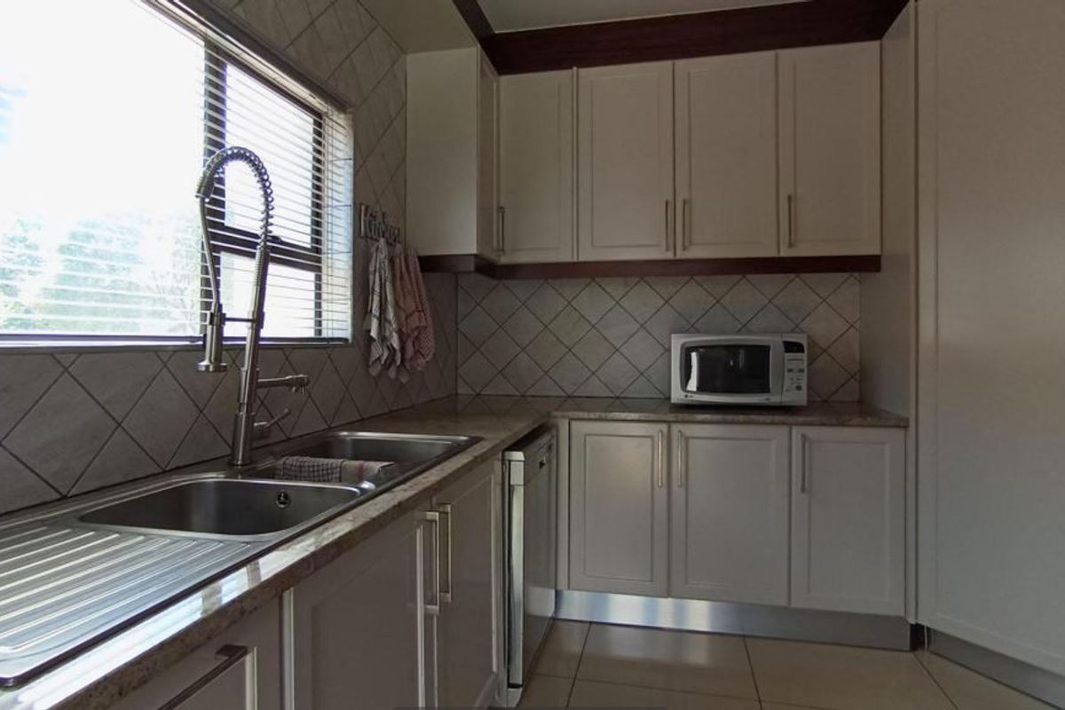 A functional kitchen featuring light-toned cabinetry, stone countertops, a double sink with a gooseneck faucet, and a tiled backsplash.
