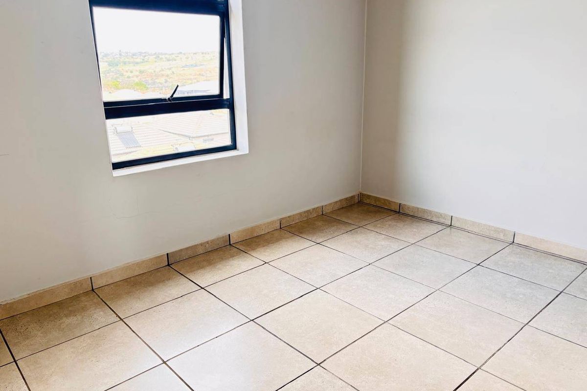 An empty bedroom featuring neutral tiled flooring, clean walls, and an aluminium-framed window with a view.