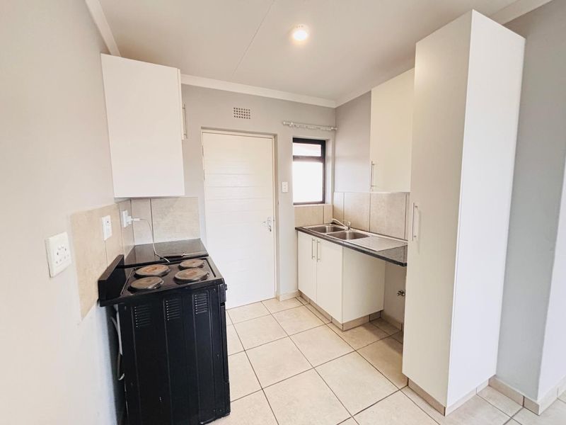 A functional kitchen featuring white cabinetry, tiled flooring, a double sink, and a standalone electric stove with a tiled backsplash.