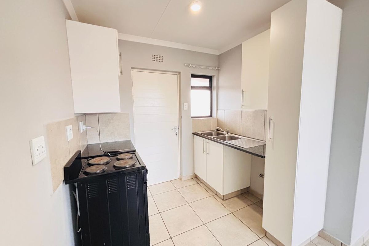 A functional kitchen featuring white cabinetry, tiled flooring, a double sink, and a standalone electric stove with a tiled backsplash.