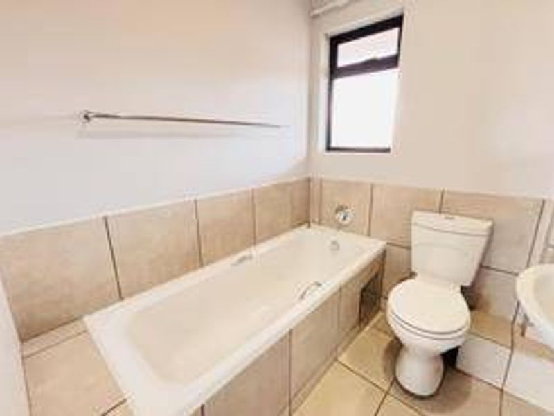A functional bathroom featuring a bathtub, pedestal basin, and toilet with neutral wall and floor tiling.