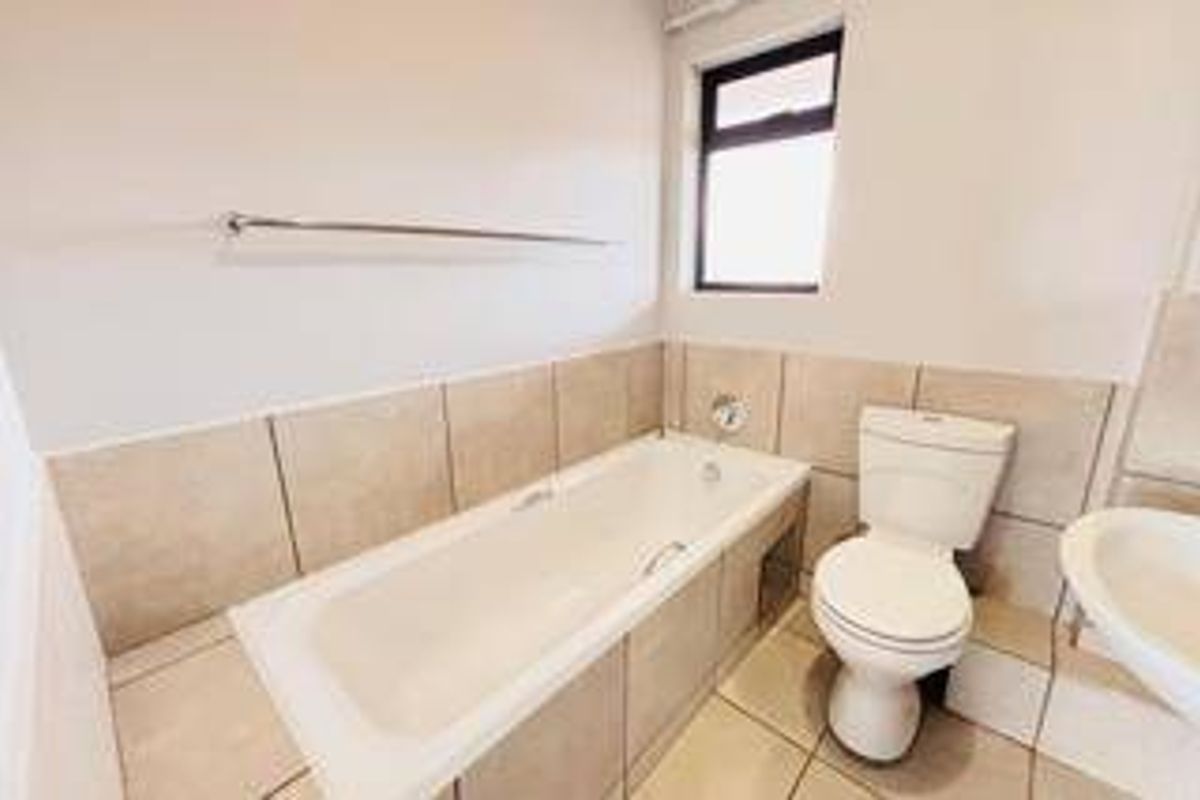 A functional bathroom featuring a bathtub, pedestal basin, and toilet with neutral wall and floor tiling.