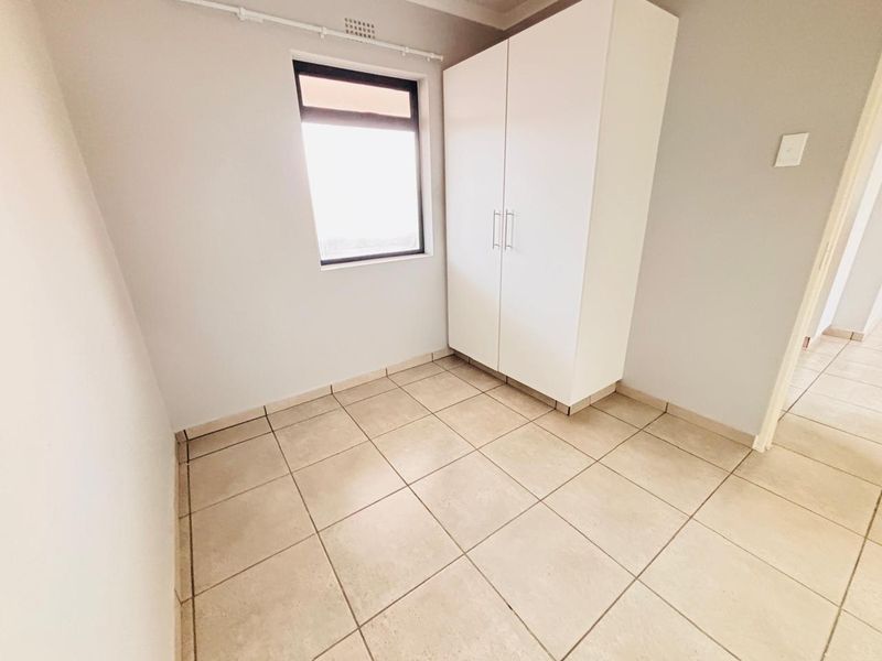 A clean, empty bedroom featuring neutral tiled flooring, a built-in white wardrobe, and a window providing natural light.