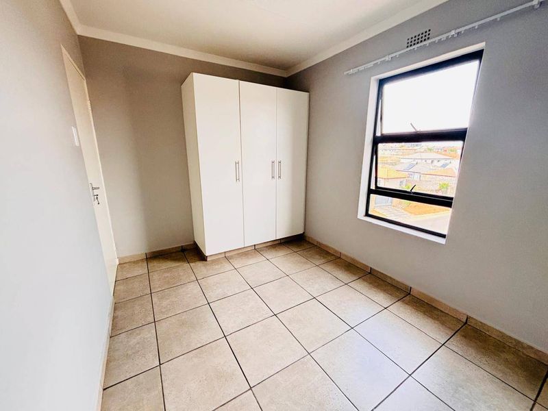 A clean, empty bedroom featuring neutral wall paint, tiled flooring, and a built-in wardrobe with ample natural light from the window.